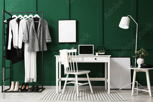 Interior of modern room with workplace, rack and blank photo frame on green wall © Pixel-Shot