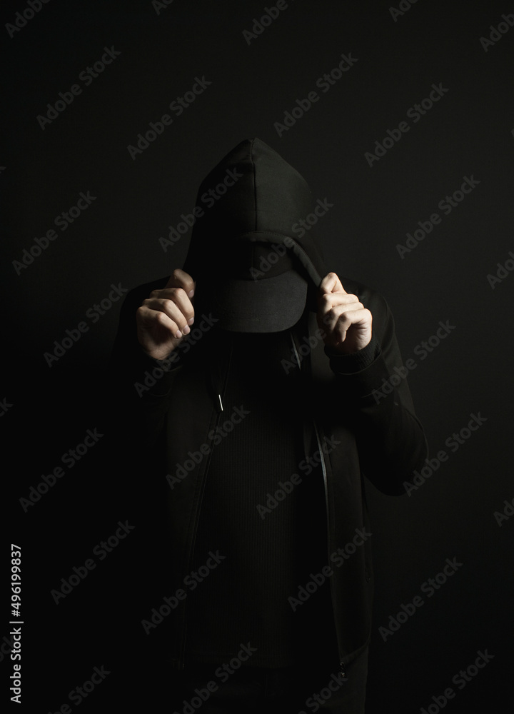 Plakat Man standing alone in the dark wearing a black hoodie and