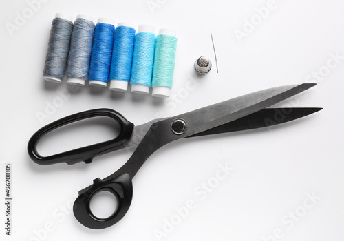 Thread spools with scissors and needle on white background