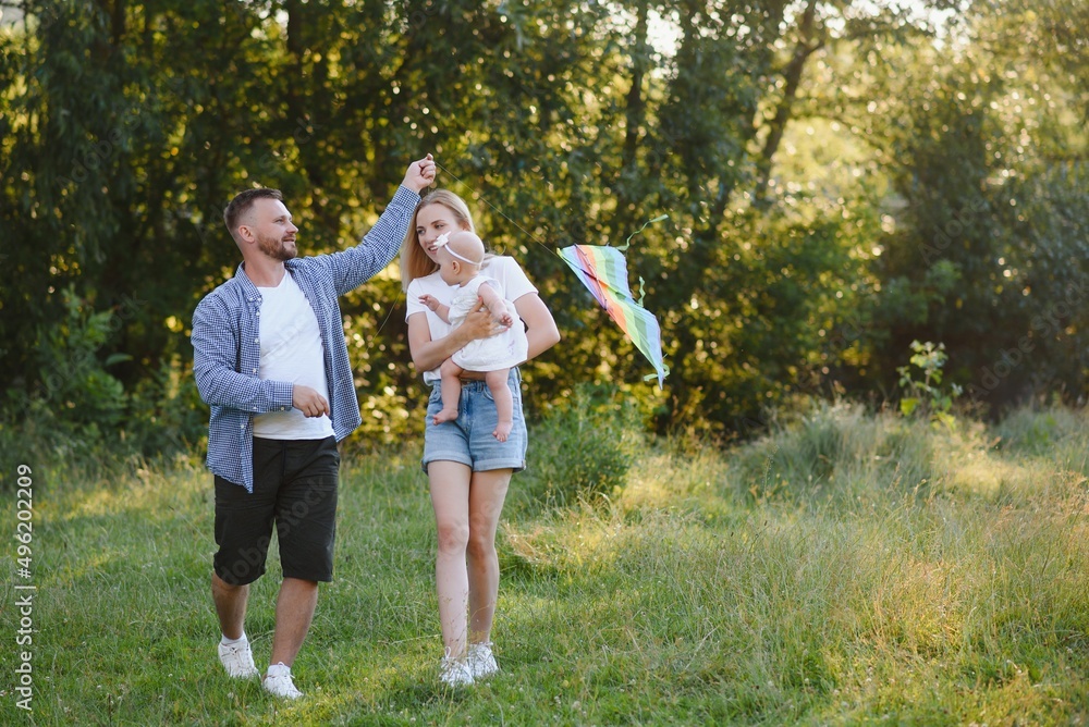 Obraz premium Young beautiful family with a little daughter hug, kiss and walk in nature at sunset. Photo of a family with a small child in nature.