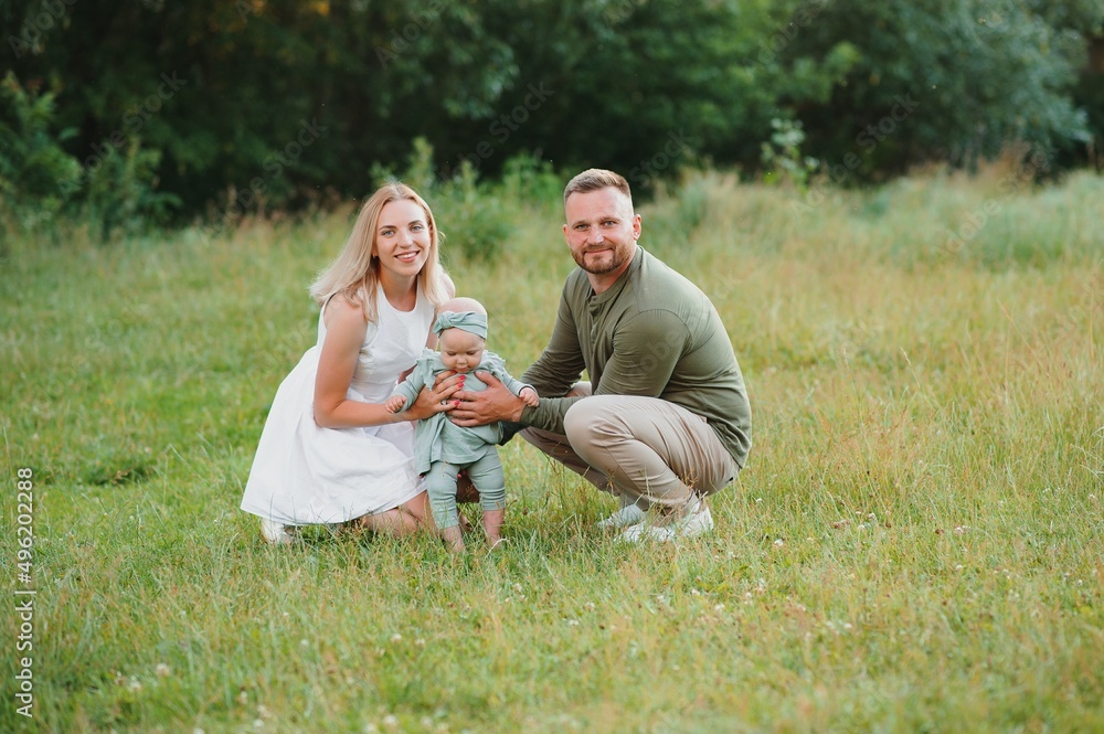 Fototapeta premium Young beautiful family with a little daughter hug, kiss and walk in nature at sunset. Photo of a family with a small child in nature.