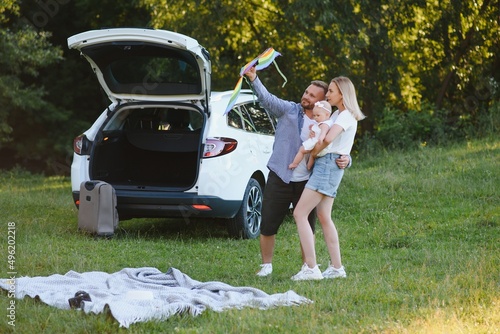 Young family three people in white clothes have picnic. Beautiful parents and daughter travel by car during summer vacation. Scene in park