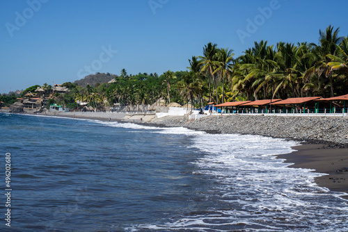 View in touristic village in El Tunco, El Salvador. Huts and palm trees on the shore of Pacific Ocean
