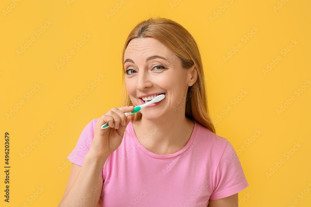Beautiful mature woman brushing teeth on yellow background Beautiful mature woman brushing teeth on yellow background