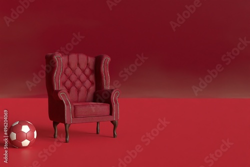 Red velvet armchair of old design on short legs with a football ball on red background. 3d rendering