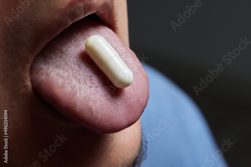 Man taking pill, mouth open with tongue sticking out.