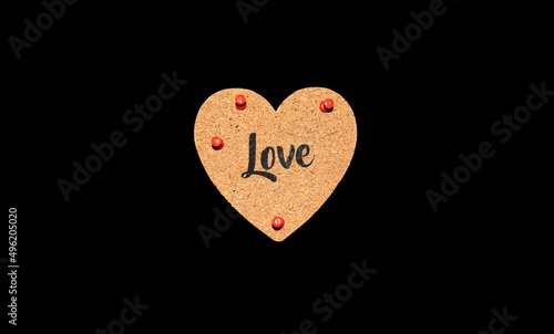 Isolated cork heart with the word "Love" and red pins against a dark black background.