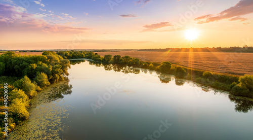 Amazing view at scenic landscape on a beautiful river and colorful sunset with reflection on water surface and glow on a background, spring season landscape