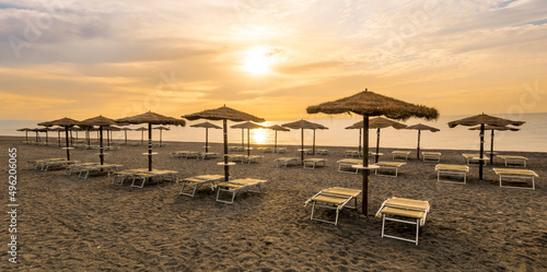  empty beach during beautiful sunrise or sunset with chaise loungues and nice umbrellas with blue sea  sun glow and amazing cloudy sky on thr background