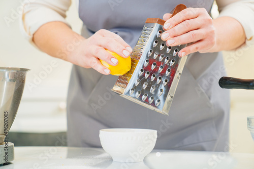 a woman cook makes lemon zest on a grater to make pastries or cream.  photo