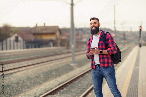 Portrait of young caucasian man using mobile phone at train station.