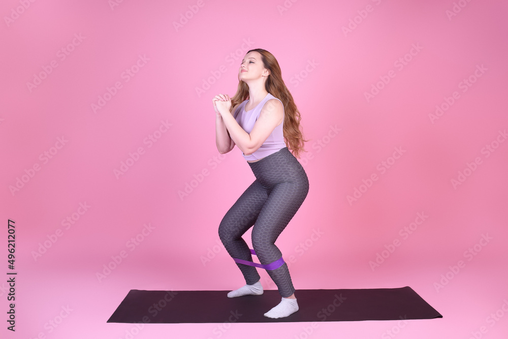 A beautiful body-positive girl on a pink background in a full-length sports suit goes in for sports, elastic bands for training, leg exercises, fitness A beautiful body-positive girl on a pink background in a full-length sports suit goes in for sports, elastic bands for training, leg exercises, fitness