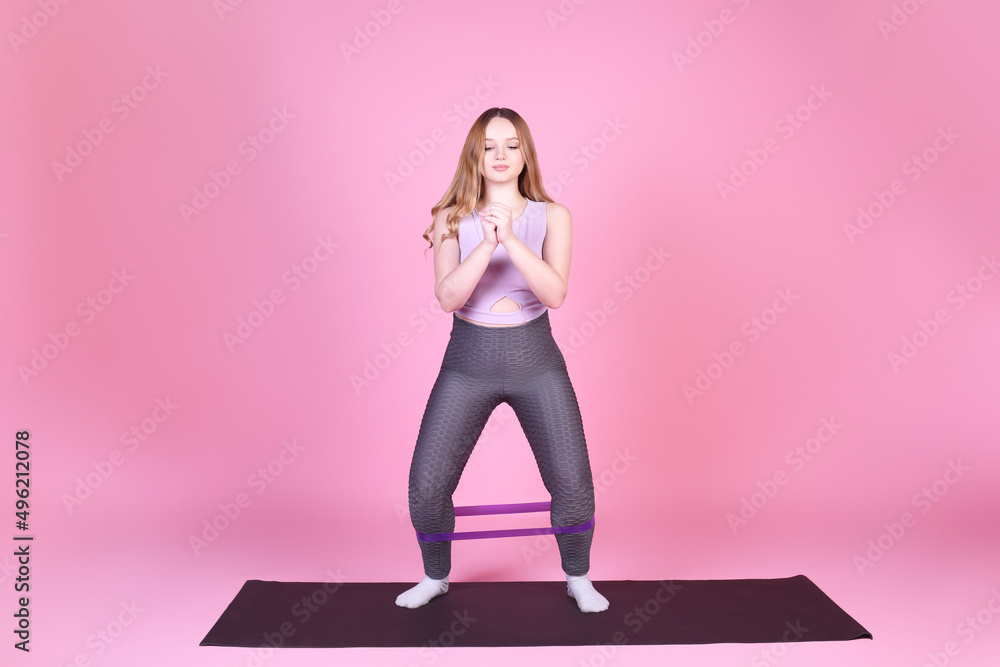 A beautiful body-positive girl on a pink background in a full-length sports suit goes in for sports, elastic bands for training, leg exercises, fitness A beautiful body-positive girl on a pink background in a full-length sports suit goes in for sports, elastic bands for training, leg exercises, fitness
