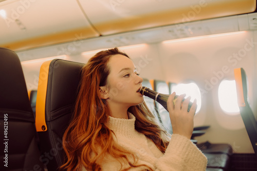 The girl in the plane drinks champagne alcohol from excitement. Fear of flying on an airplane.