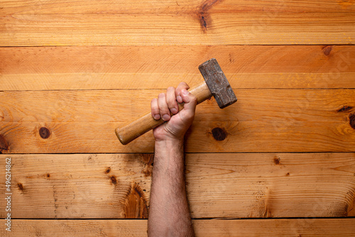 Arm holding sledgehammer on light wooden background - Labor Day