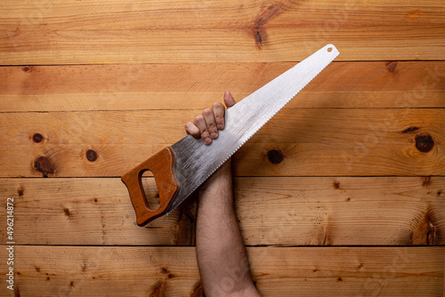 Arm holding woodworking hand saw on light wood background - Labor Day