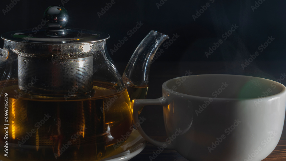Picture of glass teapot with ceramic cup of green tea on dark background. Hot chinese green tea. Picture of glass teapot with ceramic cup of green tea on dark background. Hot chinese green tea.