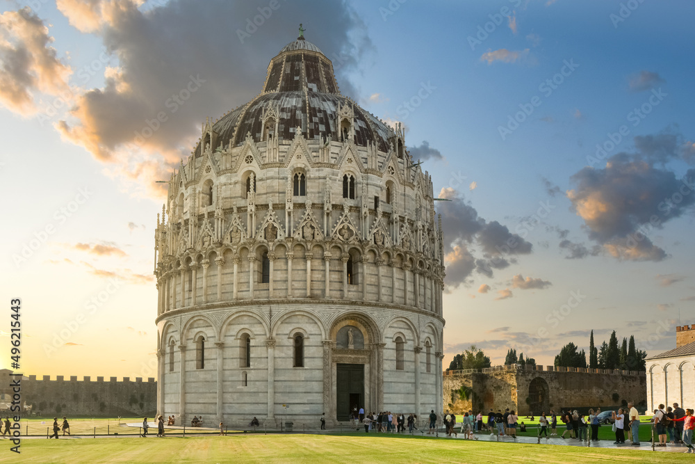 Sunset on the Piazza dei Miracoli or Field of Miracles as tourists sightsee near the Baptistery of St. John in Pisa Italy