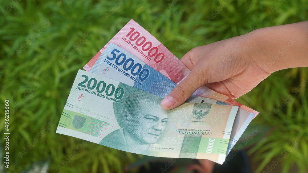 The Indonesian currency, the 20,000, 50,000 and 100,000 rupiah notes, are held in the hands of a woman