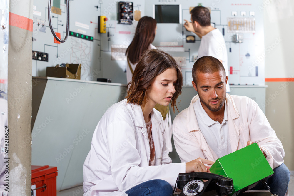 Obraz premium Focused girl and guy checking battery charger while trying to get out of escape room stylized as underground shelter