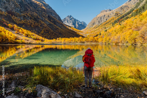Hiker woman at lake in autumnal mountains. Mountain lake and tourist with backpack