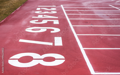 The starting line on a red running track with the lane numbers from eight to one painted in white. photo