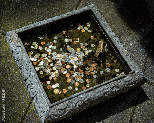 A top view of a wishing well with gold, silver and bronze coins at the bottom, covered in green water. Nice stone well ornated. photo