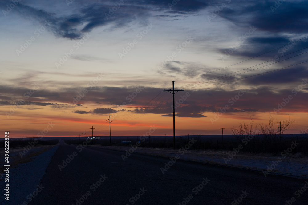 Power lines leading to a colorful sunset sky along a country road