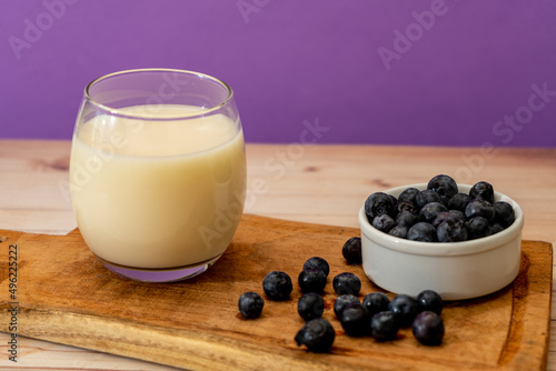 High view of a glass of milk next to some organic blueberries in a modern, stripped-down setting. Healthy eating