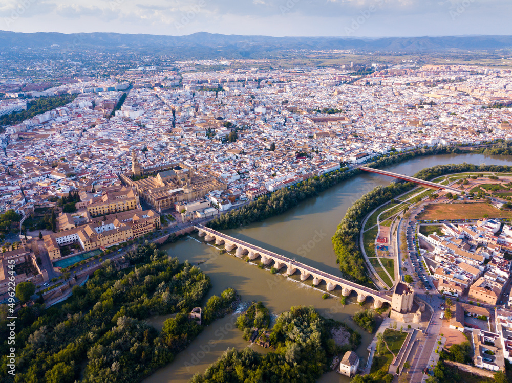 Aerial panoramic view of modern Cordoba cityscape on banks of Guadalquivir River with ancient pedestrian Roman Bridge and Mosque-Cathedral, Spain.