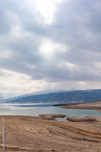 A beautiful reservoir in the mountains. Low water level  drought and beautiful patterns are visible along the banks. A red pleasure boat is standing by the shore