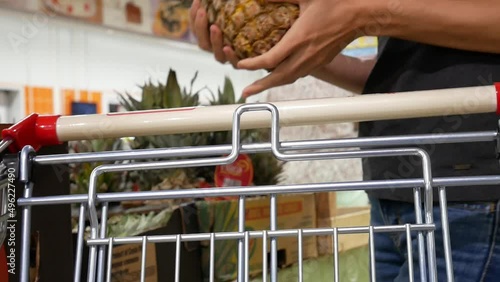 A beautiful girl puts a big ripe pineapple in a shopping cart in supermarke photo
