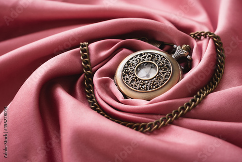 The vintage watch necklace is placed on the pink gold fabric
