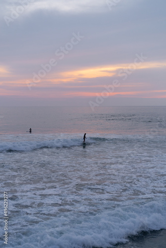 Surfers catch waves at sunset in the ocean. Surfing background