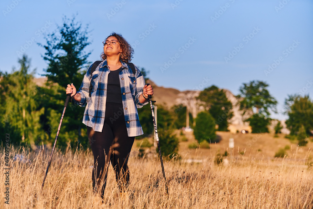 A woman hiking with a backpack and poles at sunset. Selective focus