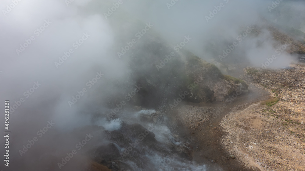 The eruption of a geyser. Water boils in a stone cauldron on the hillside. There are splashes and thick steam in the air. A river flows from hot springs in the valley. Kamchatka. Valley of Geysers