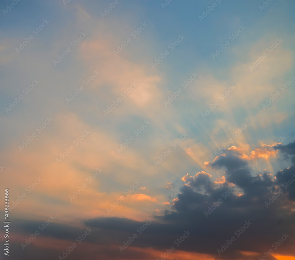 Blue and orange sunset sky with rays of sun. Sun rays slipping through clouds while sun sets.