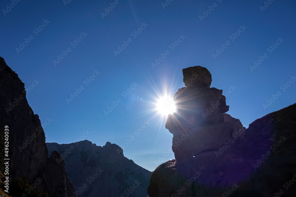 The sun is hiding behind a pile of rock in the scenic region of the Hochschwab mountain in Styria, Austria, Europe. The sun rays and sun beams are scattering on the stones. Lens flare photography