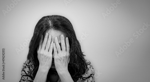 Asian senior woman with hands covering her face in black and white color filter