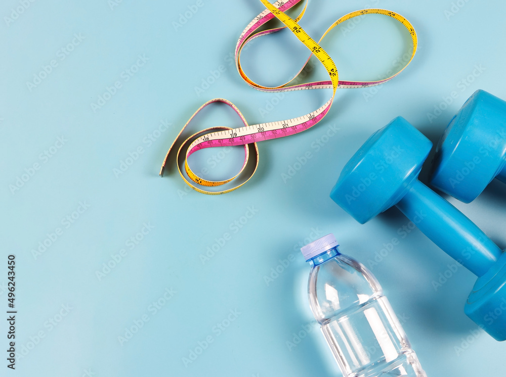 flat lay of blue dumbbells, measuring tape and bottle of water on blue background with copy space. Self development and active lifestyle concept. flat lay of blue dumbbells, measuring tape and bottle of water on blue background with copy space. Self development and active lifestyle concept.