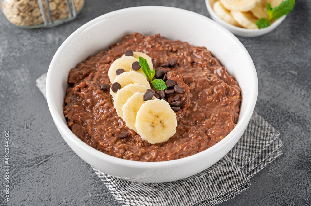 Chocolate oatmeal porridge with banana and chocolate chips on top in a white bowl. Healthy breakfast. Copy space. Chocolate oatmeal porridge with banana and chocolate chips on top in a white bowl. Healthy breakfast. Copy space.