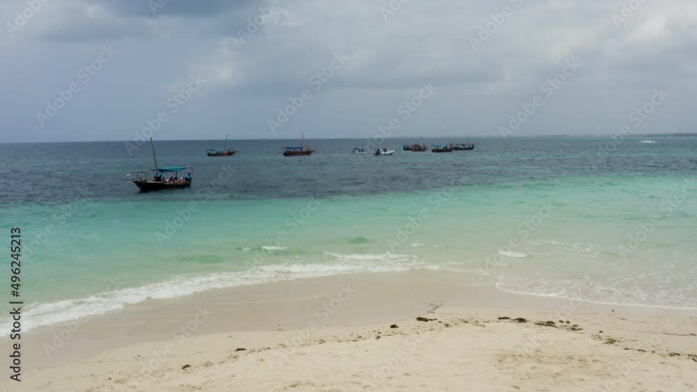 Boats anchored just offshore white sand beach in Zanzibar, one sailing.