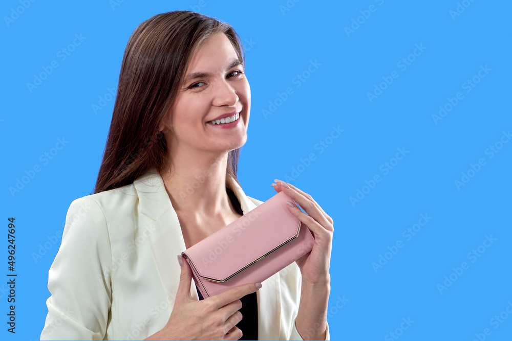 Obraz premium A beautiful young woman is holding a pink purse on a blue background, copy space