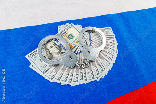 silver metal police handcuffs over paper dollar banknotes of United States of America over national flag of Russian Federation photo