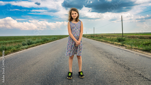 Teenage girl standing allone on a road middle of a plain landscape photo