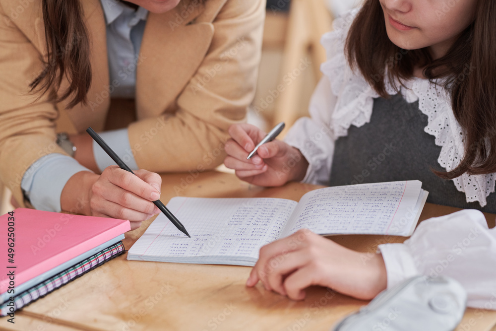Close up of unrecognizable female teacher helping girl during class in school, focus on pen writing in notebook Close up of unrecognizable female teacher helping girl during class in school, focus on pen writing in notebook