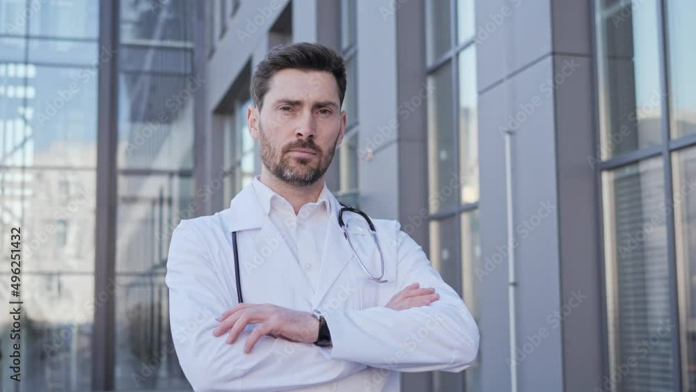 Portrait of caucasian male healthcare worker physician doctor standing outside hospital confident looking in to camera. Face of surgeon wearing scrubs and stethoscope posing on clinic background. Portrait of caucasian male healthcare worker physician doctor standing outside hospital confident looking in to camera. Face of surgeon wearing scrubs and stethoscope posing on clinic background.