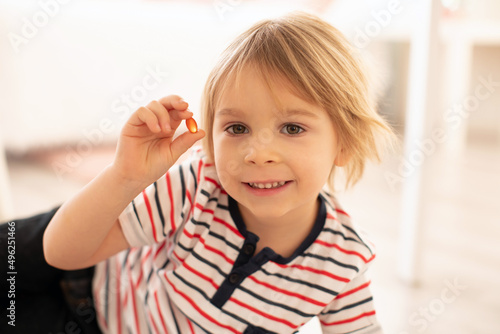 Cute little child, toddler boy, eating alfa omega 3 child suplement vitamin pills at home