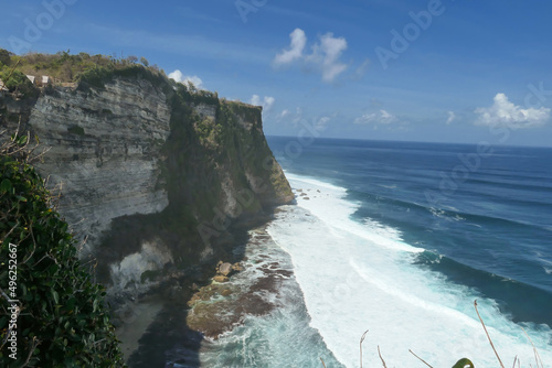 A view on Uluwatu Cliffs, Bali, Indonesia. The waves are rushing to the shore, making the water bubbly. The cliffs are overgrown with small plants and moss. Steep and dangerous fall. Hidden gem
