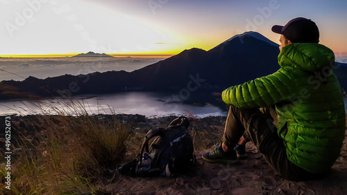 A man in a jacket sitting on top of Mount Batur, Bali, Indonesia and waiting for the sunrise. There is Mount Rinjani in the back (Lombok) and Volcano Agung on the side. Fog in the valley. Mysterious © Chris